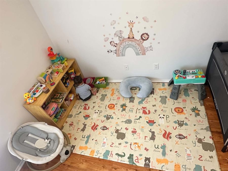 Cozy corner with an alphabet play mat, toy shelf, and travel crib for infants