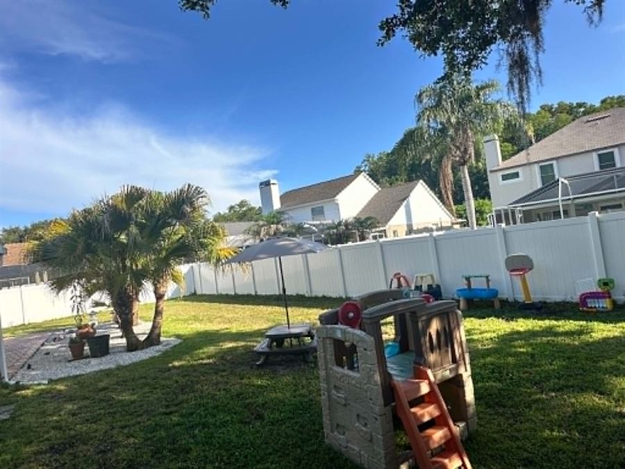 Backyard play equipment lined up along the fence with palm trees and a picnic area