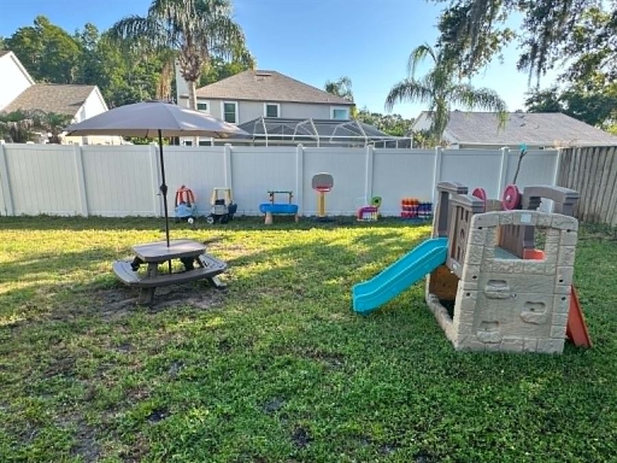 Backyard play area with a playhouse, slide, picnic table, and basketball hoop